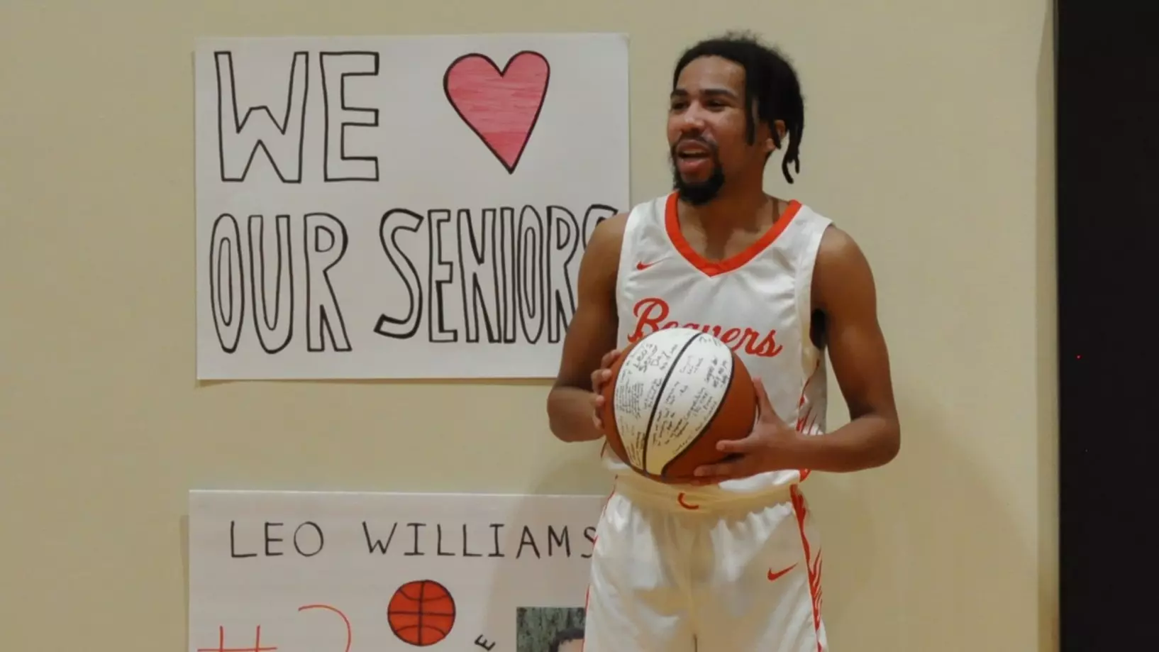 Leo Williams with an autographed basketball in front of his Senior Day posters