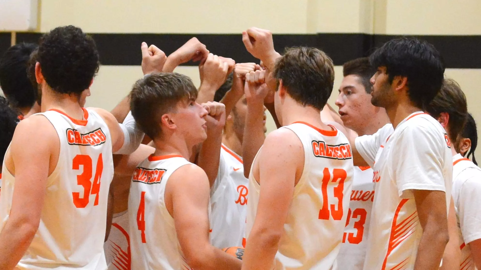 Caltech men's basketball players raise their clenched fists before breaking their huddle during a timeout
