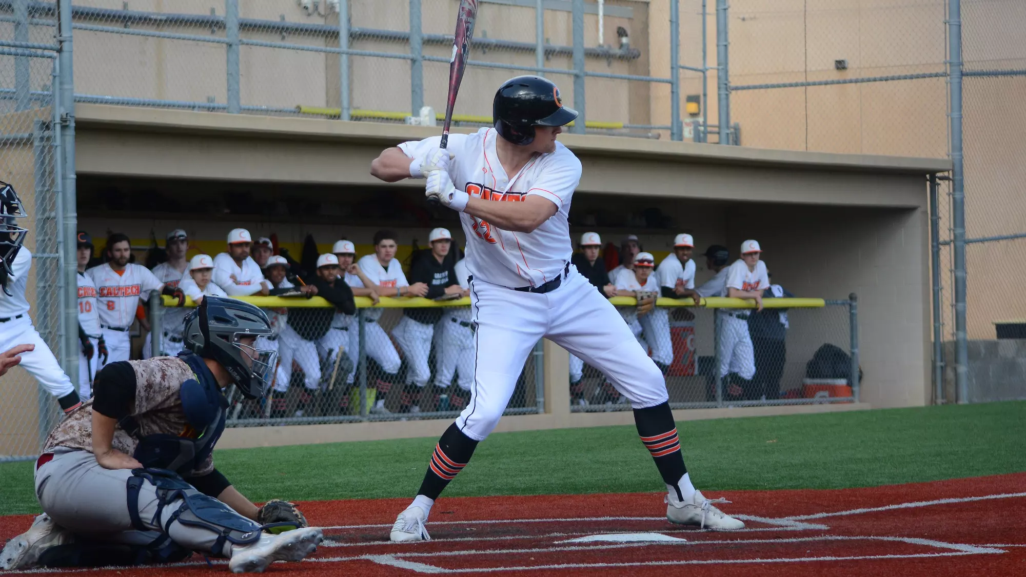 Thorsen Kristufek awaits a pitch while his teammates watch him from the Caltech dugout