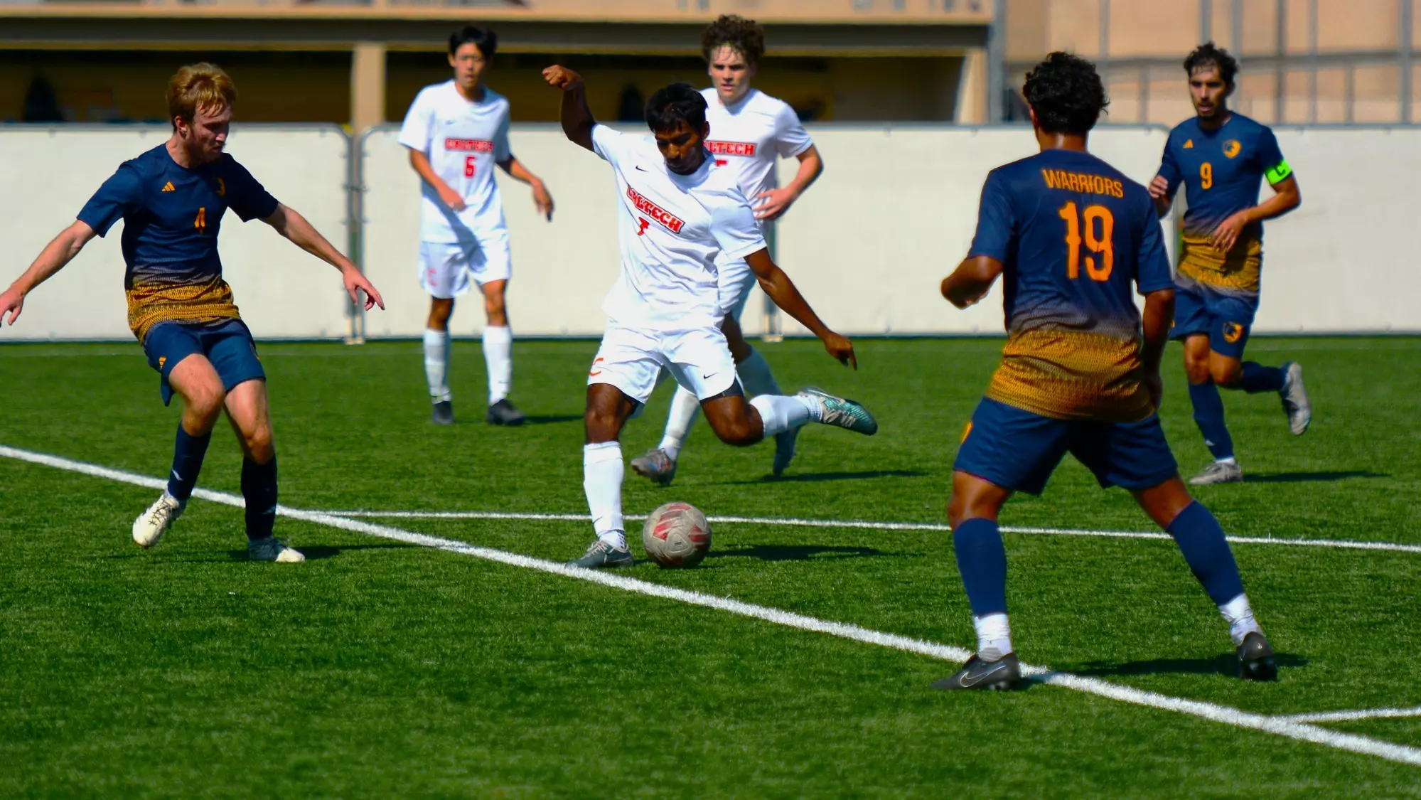 Player kicking ball with multiple defenders in the area and two teammates 