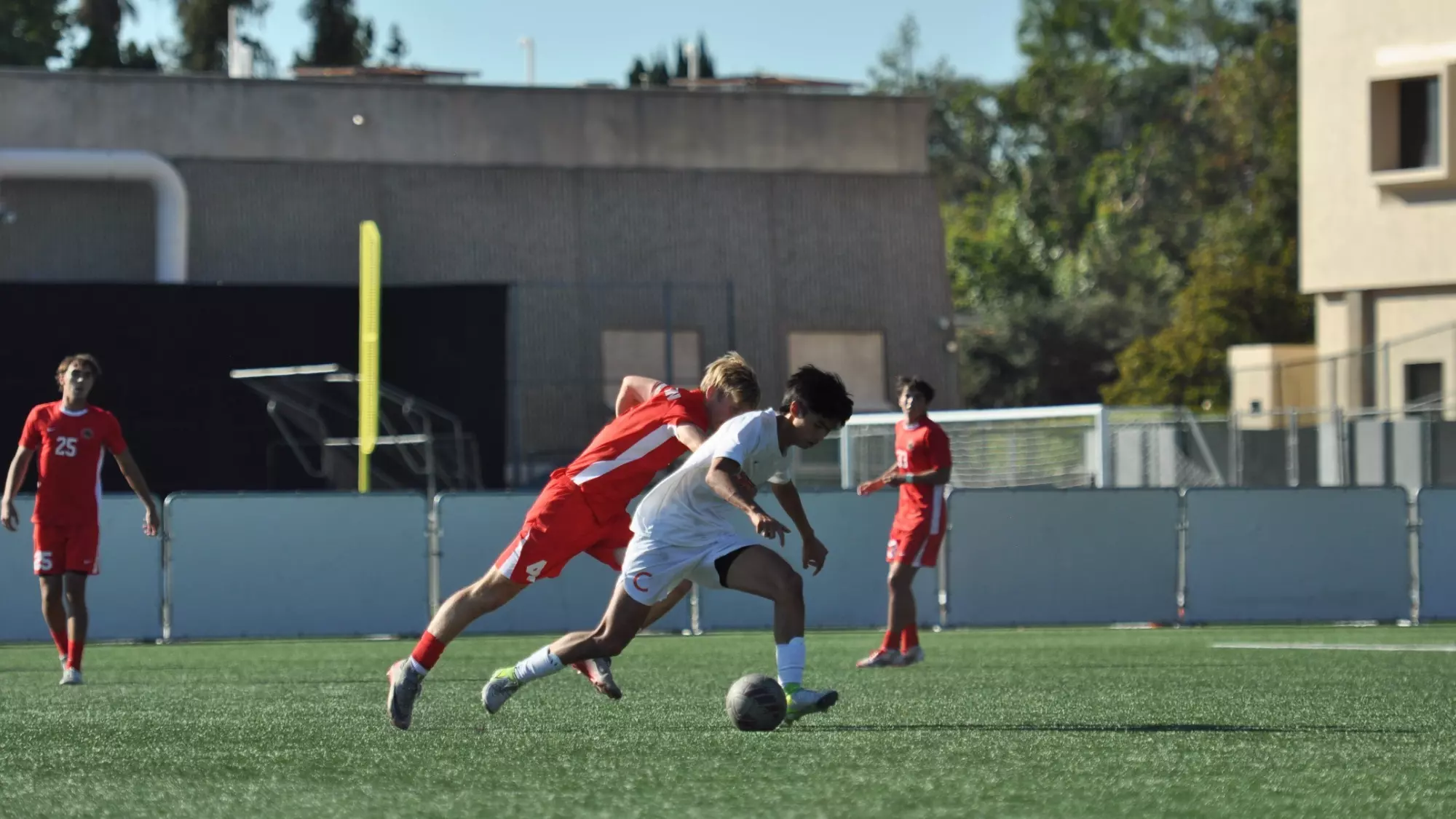 Matthew Luk, wearing white, lowers his center of gravity as he dribbles against a defender wearing red behind him. The defender reaches out, clearly beaten on the play. 