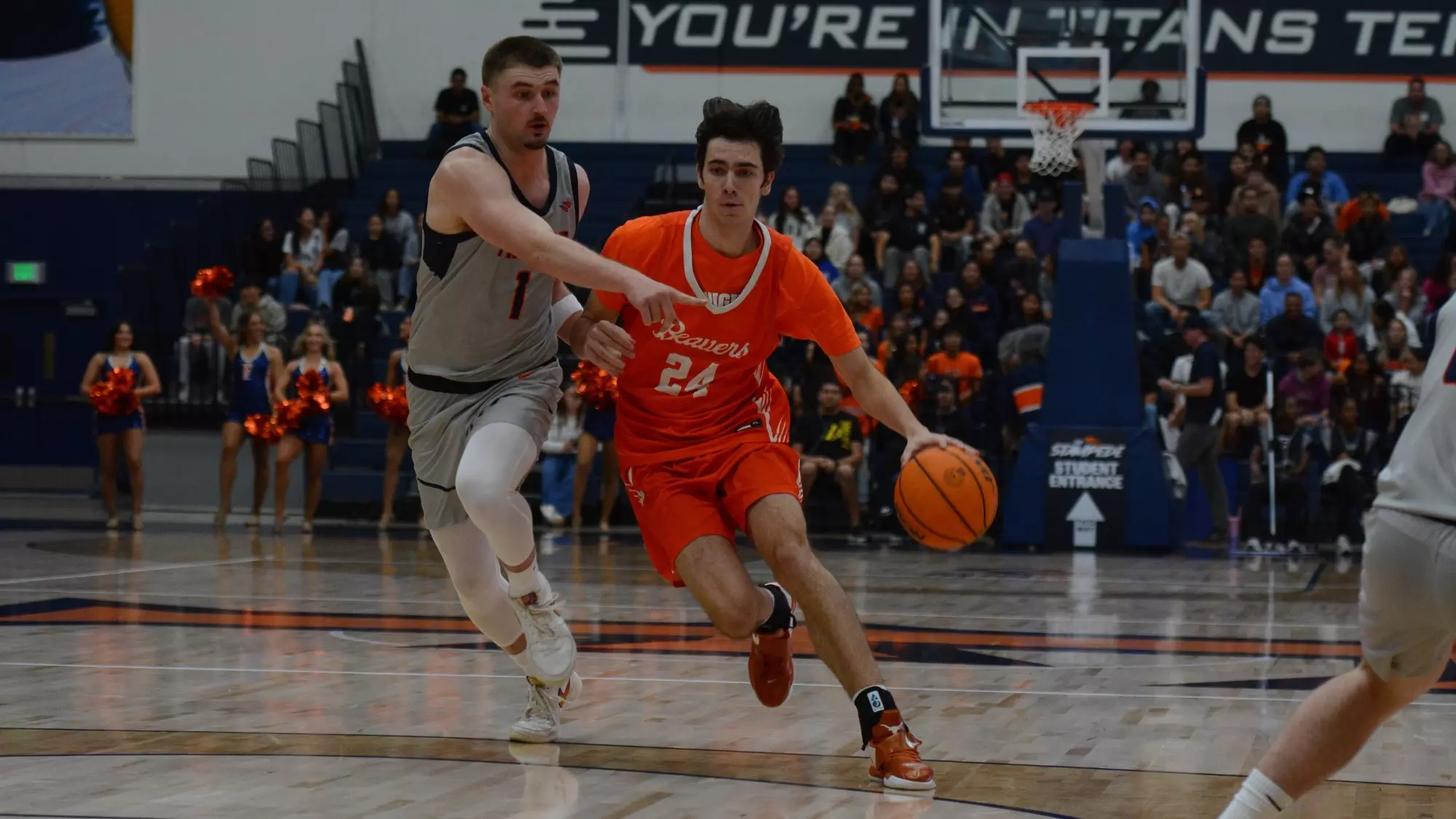 Dorian Glogovac drives towards the basket from the top of the key as viewed from under the basket. He holds the ball in his left hand while fighting off a defender with his right. 