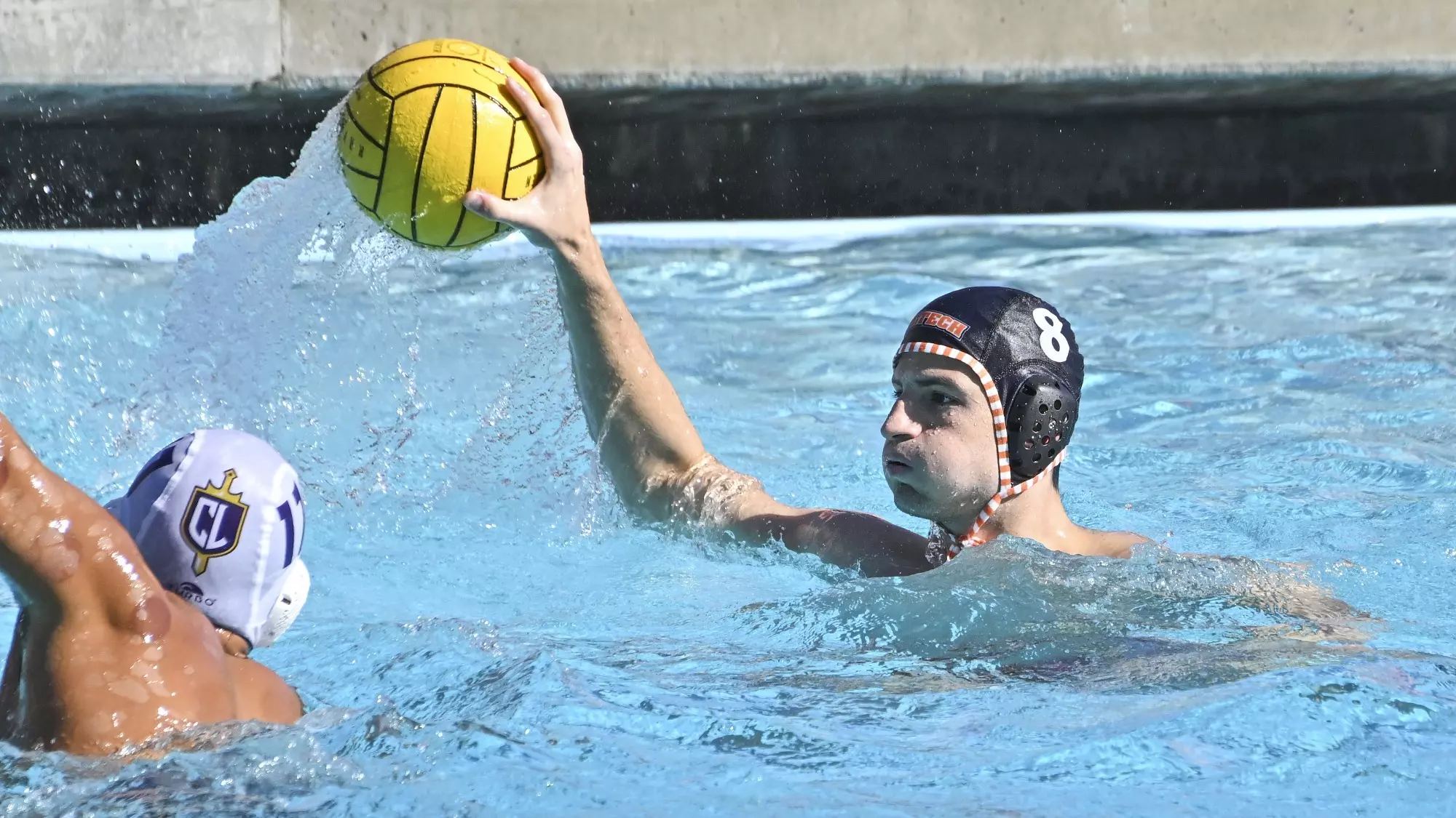 Bram Schork, wearing a dark cap, elevates the ball out of the water with his right hand while being defended by a Cal Lu player in a white cap who has suction therapy marks on his left shoulder. . 