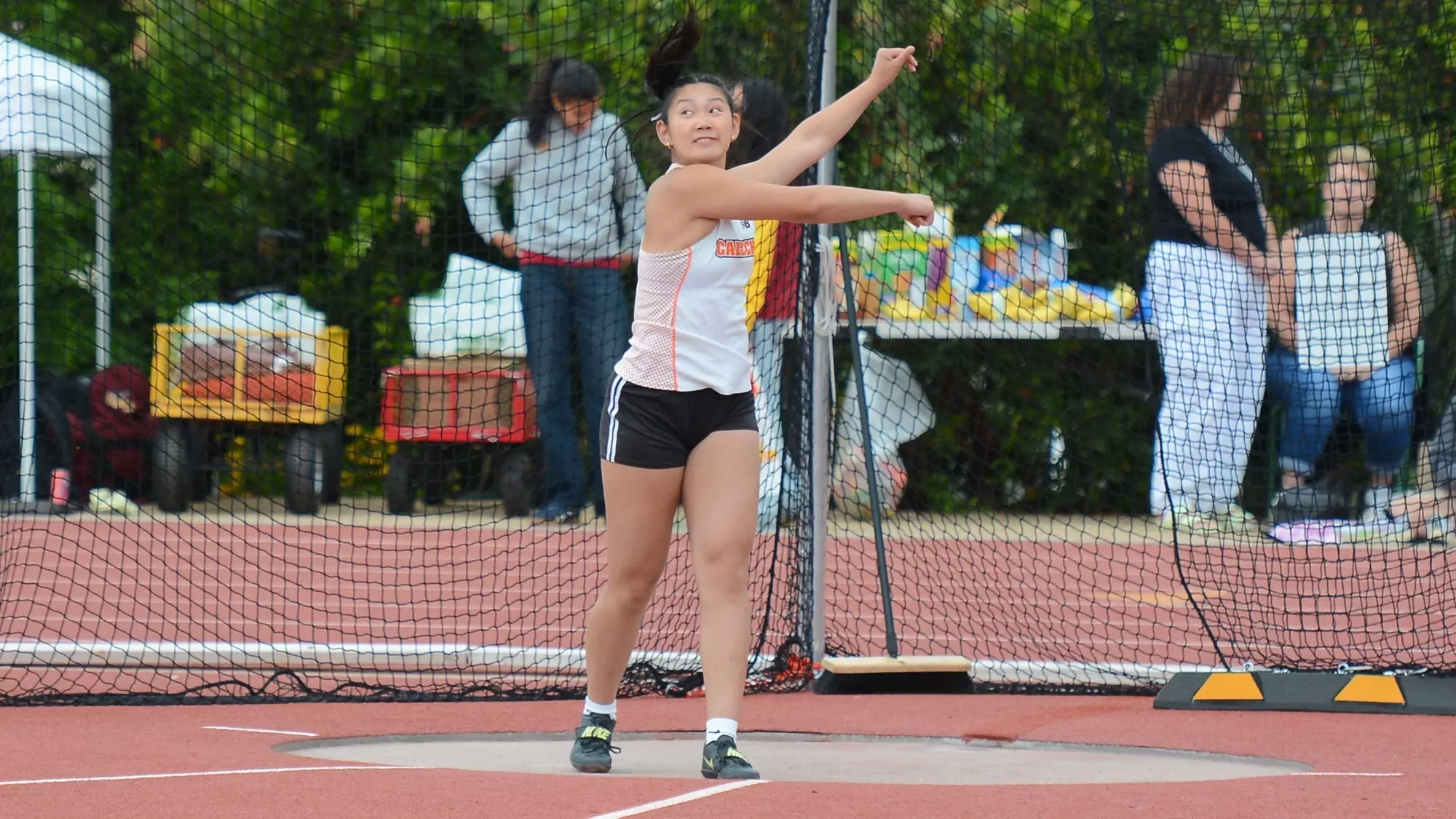 Emily Hu's arms follow through on her throw as she peers over her rotating shoulders to track her discus throw. 