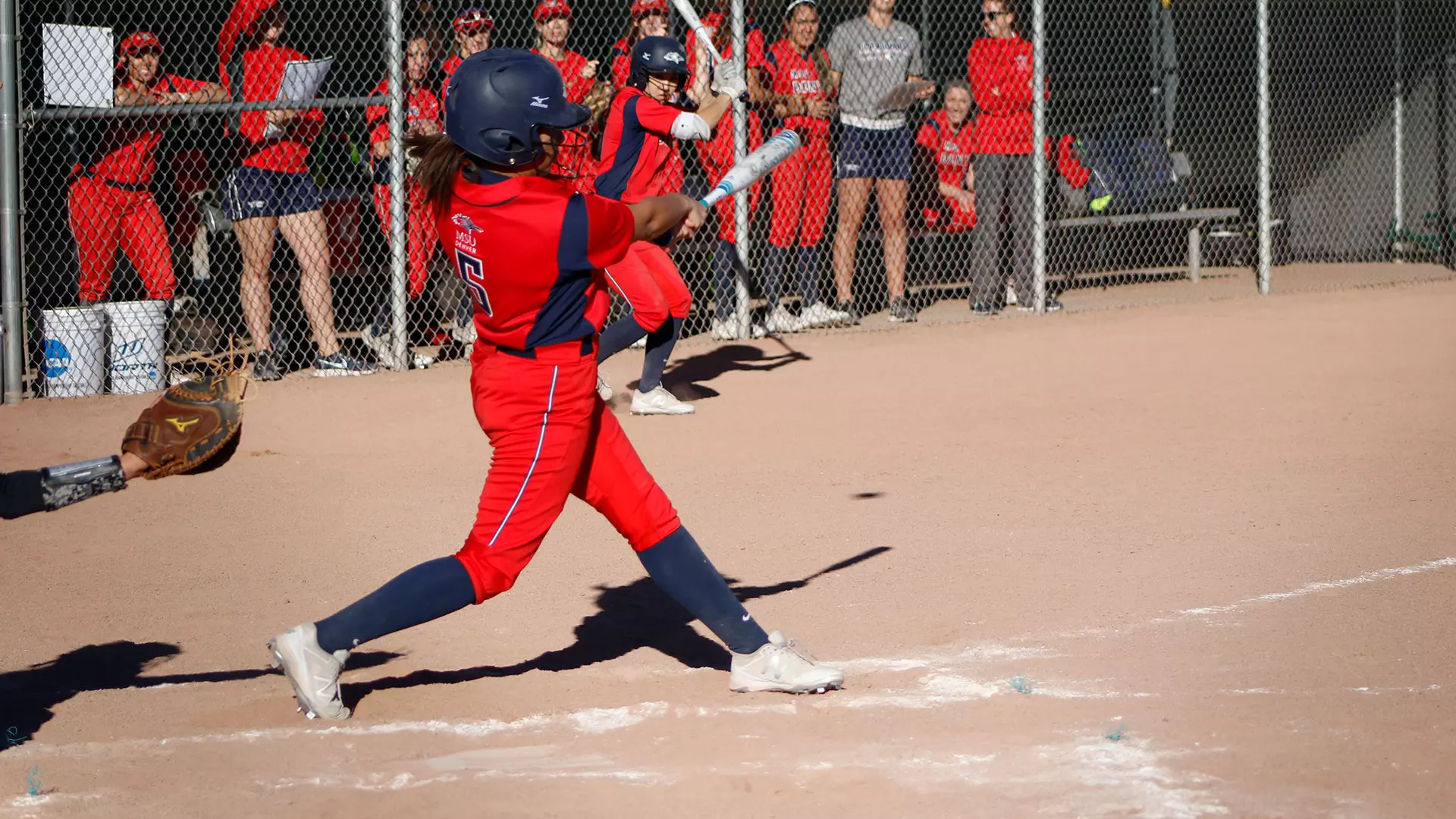 MSU Denver player  number 5 swings the bat with team in the back-round and a player on deck