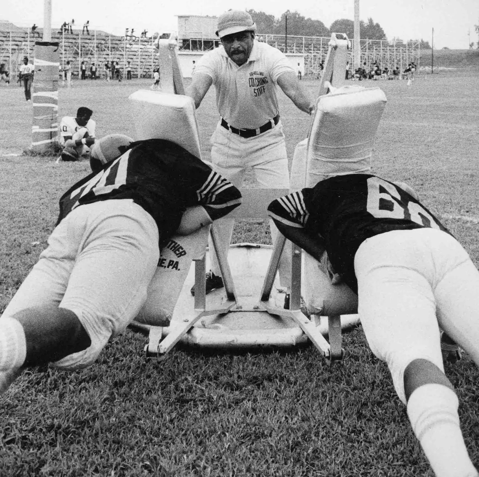 Coach Eddie Robinson stands on a 2-man sled and practices with his team.