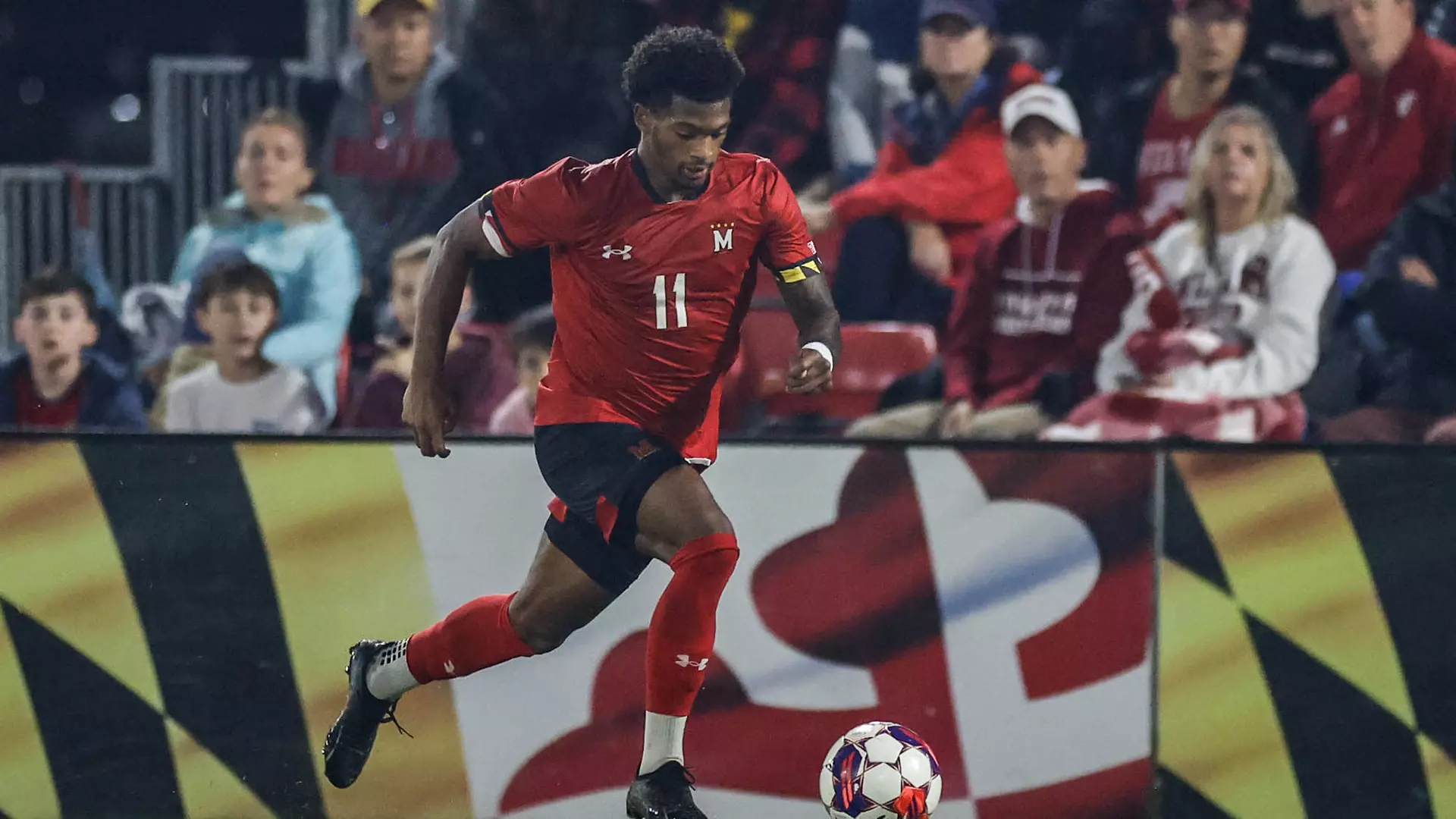 Kimani Stewart-Baynes dribbles soccer ball in red jersey at Ludwig Field