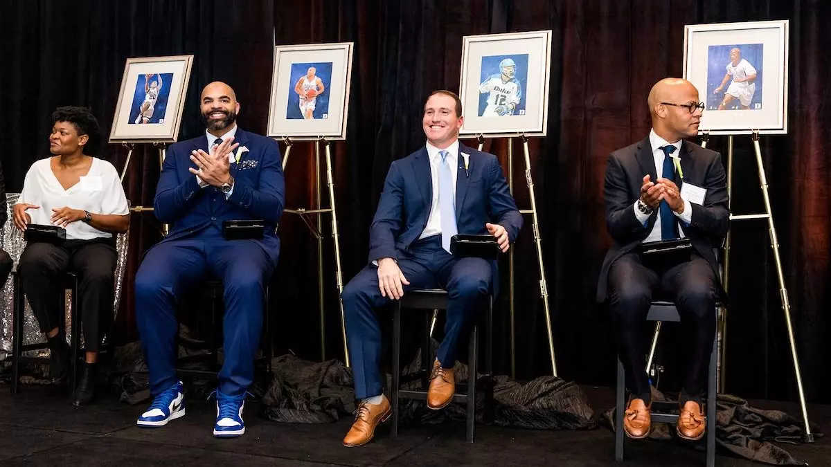 Four 2022 Duke Athletics Hall of Fame inductees sit next to their portraits during the induction ceremony