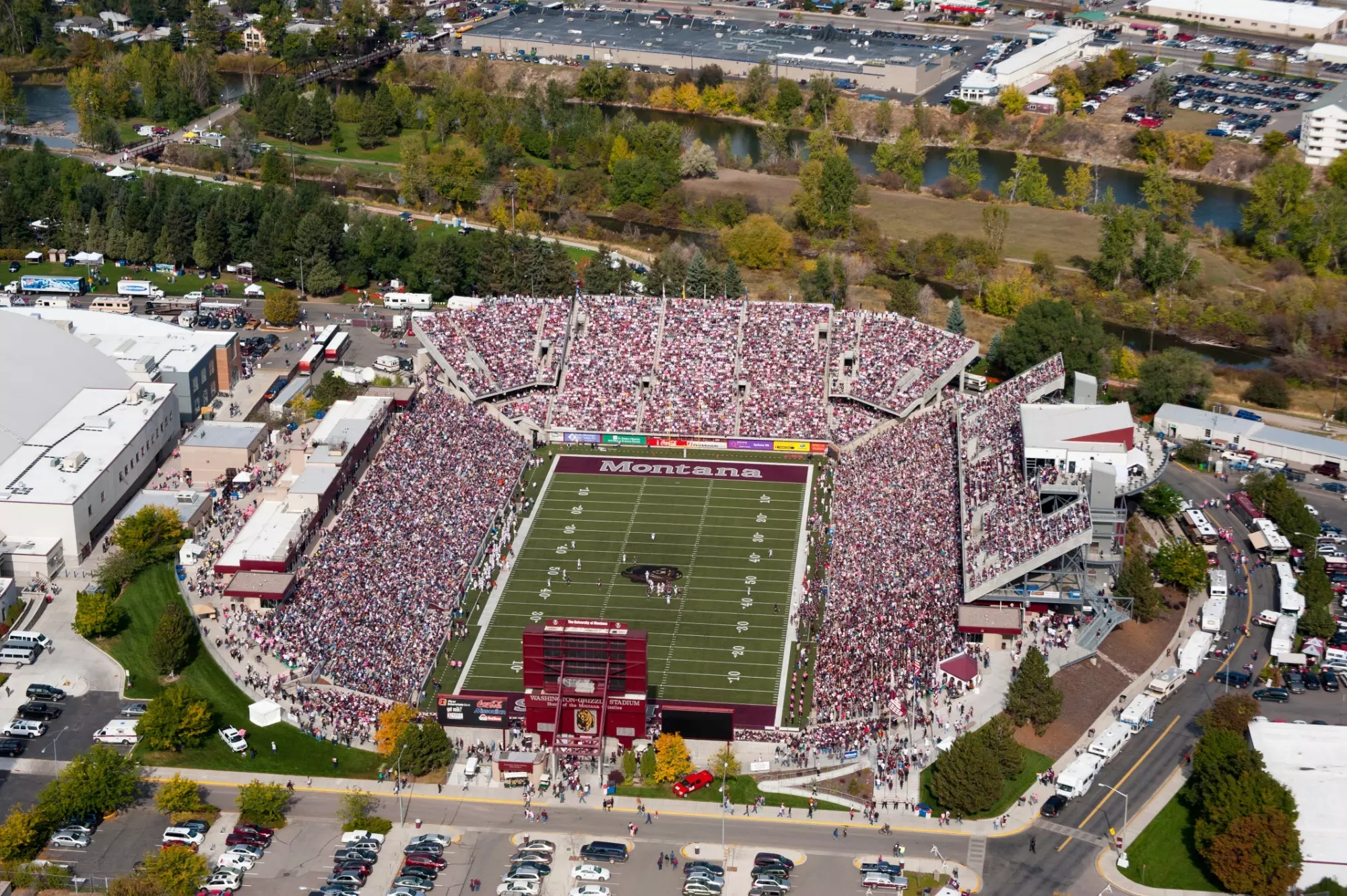 An aerial shot of a packed Washington Grizzly stadium on Griz game day with the Clark Fork River flowing by.