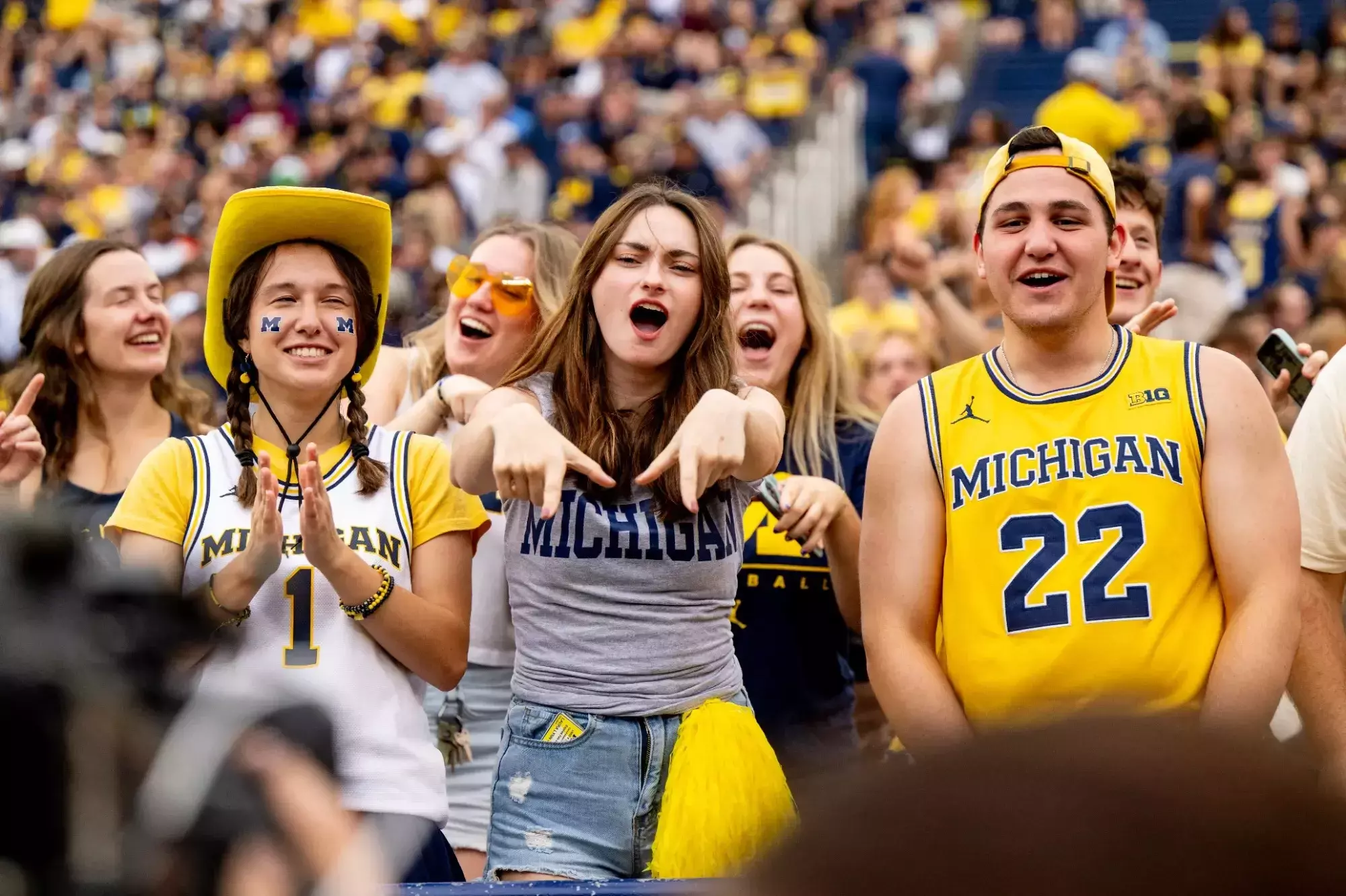 Student holds up M finger sign to camera from the student section