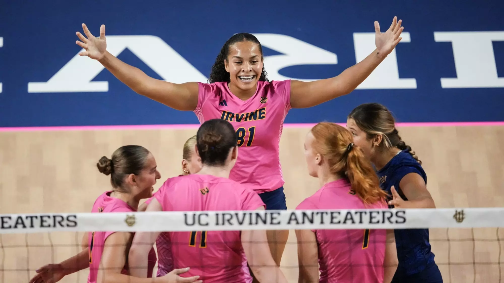 Memphis Burnett raises both arms as she celebrates a point with her teammates in an NCAA women's volleyball match.