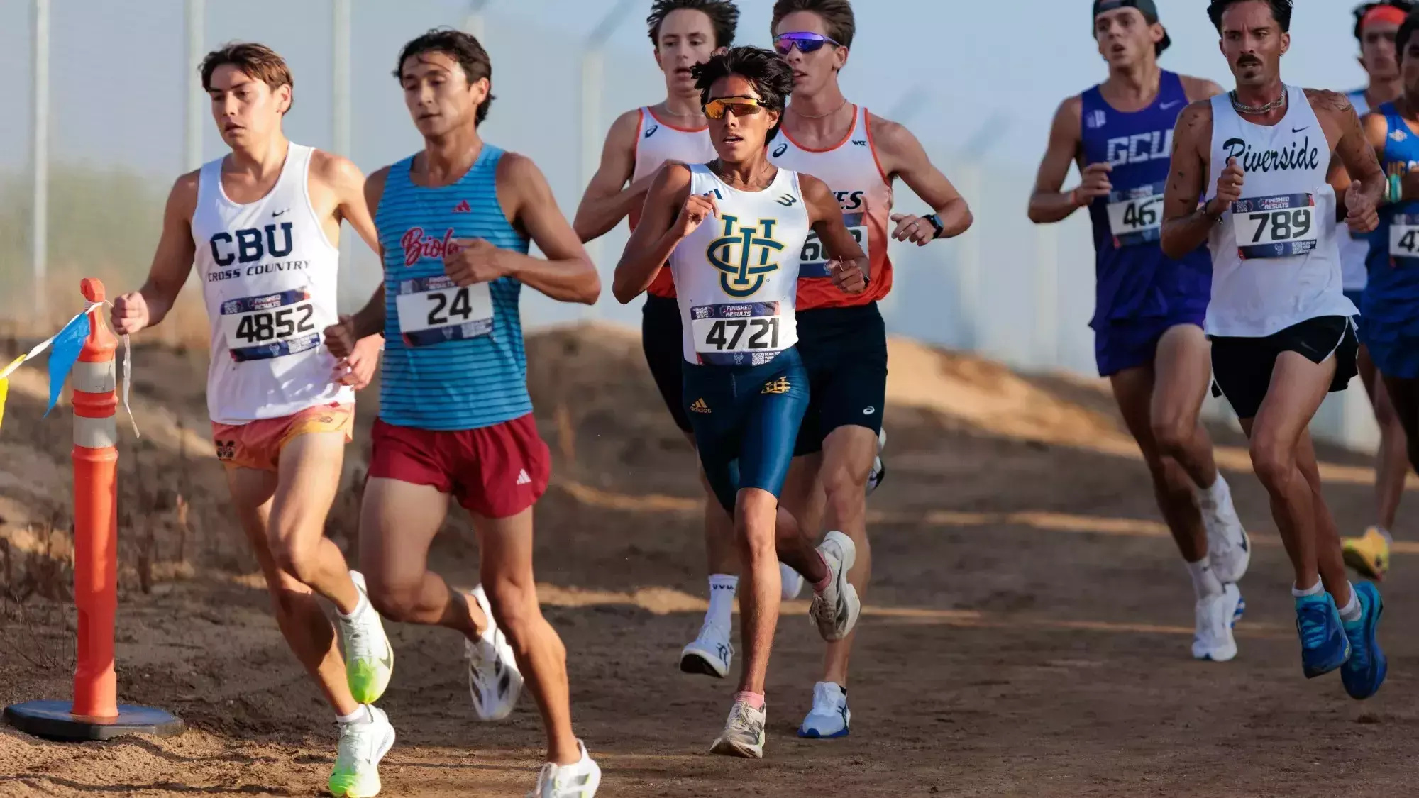 Juan Chantaca wearing a white UCI jersey and blue shorts runs in the middle of a pack during the men's 8K race at the UCR Invitational.