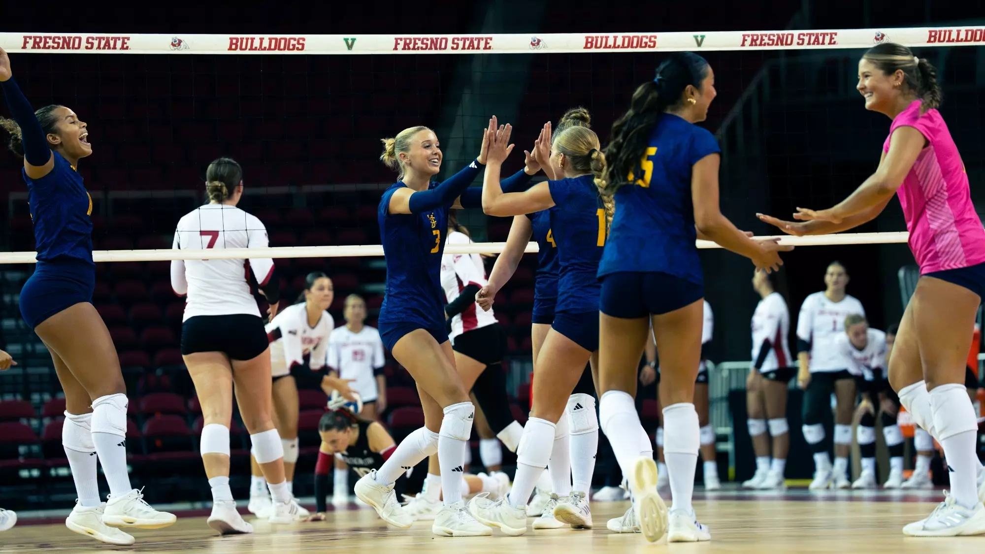 UC Irvine women's volleyball players high five and celebrate on the court after winning a point.