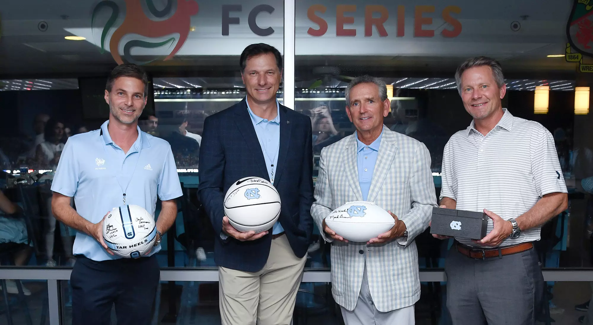 Ricardo Villar and Steve Hogan of the FC Series exchange gifts with Athletic Director Bubba Cunningham and UNC Chancellor Kevin Guskiewicz .