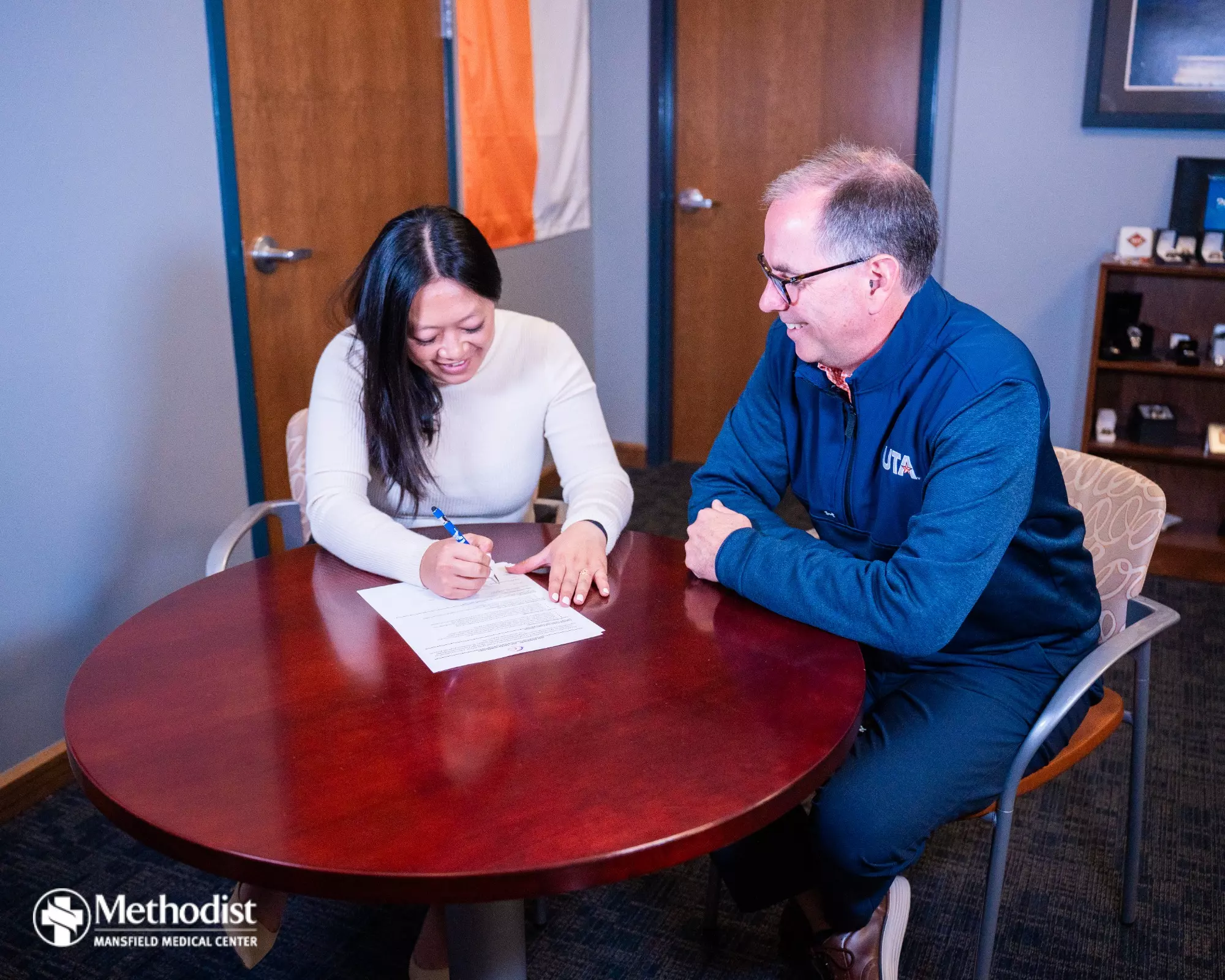 UT Arlington Flag Football Head Coach Melinda Nguyen Signs Her Contract with UTA Director of the Division of Intercollegiate Athletics Jon Fagg.