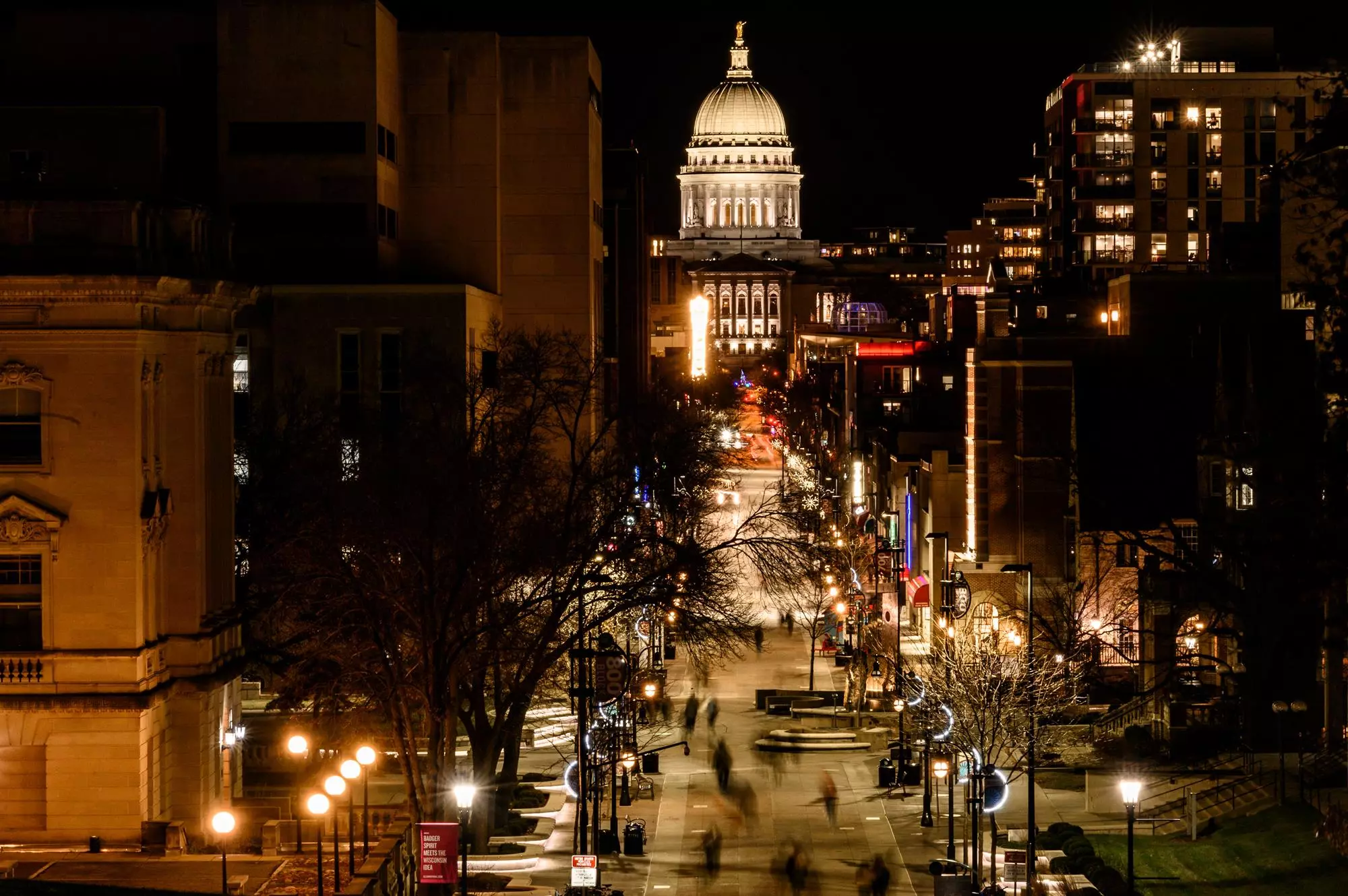 With the Wisconsin state capitol in the background, pedestrians and students walk along Library Mall and the State Street Mall at the University of Wisconsin-Madison after sunset on Dec. 4, 2019. (Photo by Bryce Richter /UW-Madison)