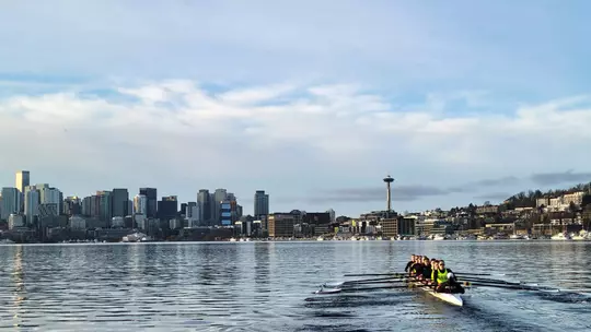 A crew of University of Washington freshman women row on Lake Union in Seattle, with the skyline and Space Needle as a backdrop