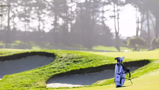 Men's golf bag sitting next to bunker