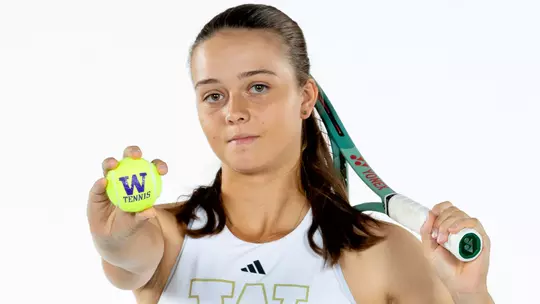 Nela Jadova holds out a tennis ball with a W and tennis written on it with a racquet over her sholder