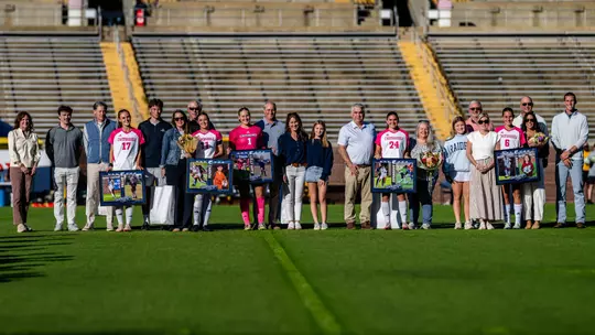 Soccer players in pink and white are with their families on the pitch before the game being honored.