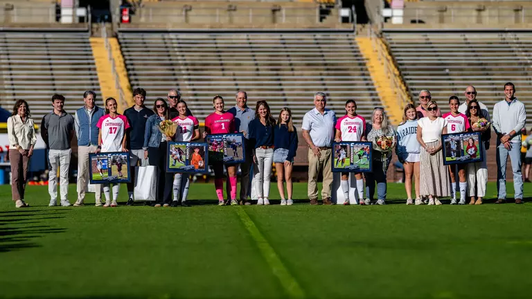 Soccer players in pink and white are with their families on the pitch before the game being honored.
