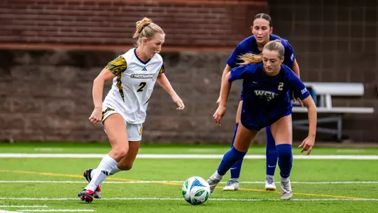 A soccer player in white is taking control of the ball against a defender in dark colors.