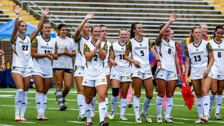 A soccer team in white is waving to the crowd after a game.