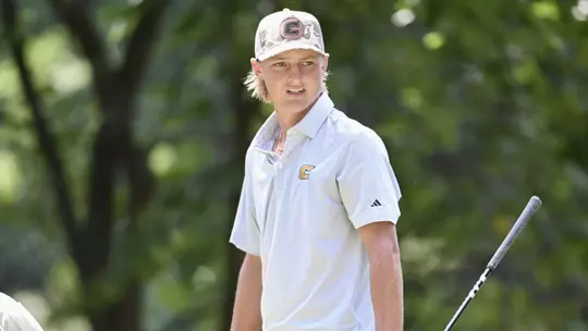 Evan Rogers walks towards his bag at the tee with his club in his left hand as he stares over his left shoulder at his ball in the fairway.