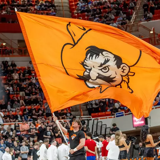 A cheerleader waves a large, orange flag showing Pistol Pete at an Oklahoma State basketball game in Gallagher-Iba Arena.