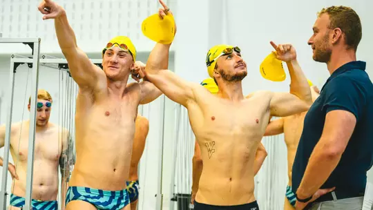 Two WVU men's swimmers flex their muscles while at practice.