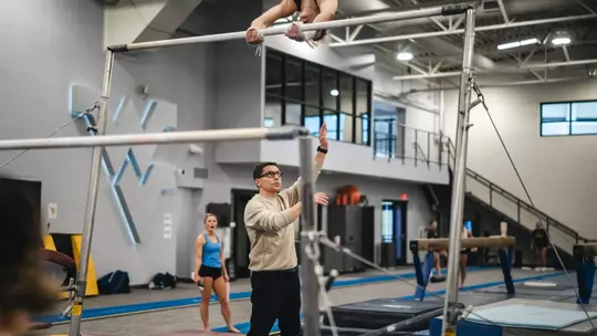 WVU gymnastics coach Jason Butts assists an athlete during practice at Cary Gym in Morgantown