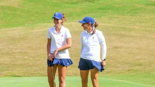 Calle Barlow and Katie Magner laugh on the putting green