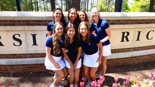 Women's golf team poses in front of a sign on campus
