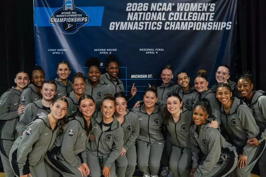 Gymnastics team in front of bracket after advancing at NCAA Tempe Regional