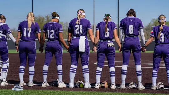 ACU softball players hold hands and bow heads in prayer before a game against UT Arlington on March 21, 2026