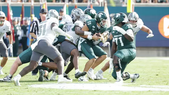 The Eastern Michigan defense swarms the Michigan State quarterback inside Spartan Stadium.