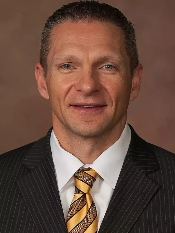 Head Football Coach Jeff Monken Headshot with a black suit and gold tie on.
