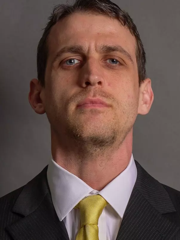 Eddie Hernon is posed with a black suit and gold tie.