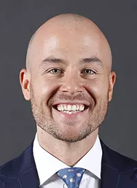 Head shot of Luke Murray wearing a blue suit and tie.
