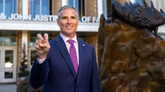 Mike Buddie gives a Go Frogs hand sign in front of Schollmaier Arena