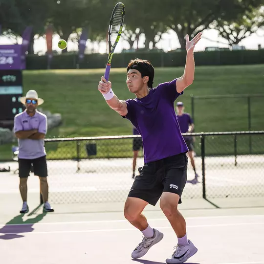 Duncan Chan prepares to connect on a volley at the net while wearing a purple shirt