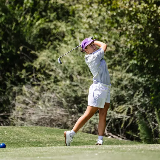 Claire Swathwood follows through on a tee shot with an iron while wearing a gray shirt