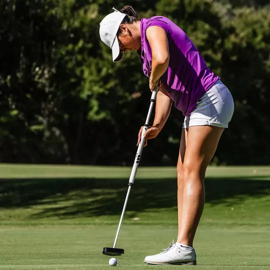 Gracie McGovern connects with a golf ball using a sweeper putter and wearing a magenta shirt