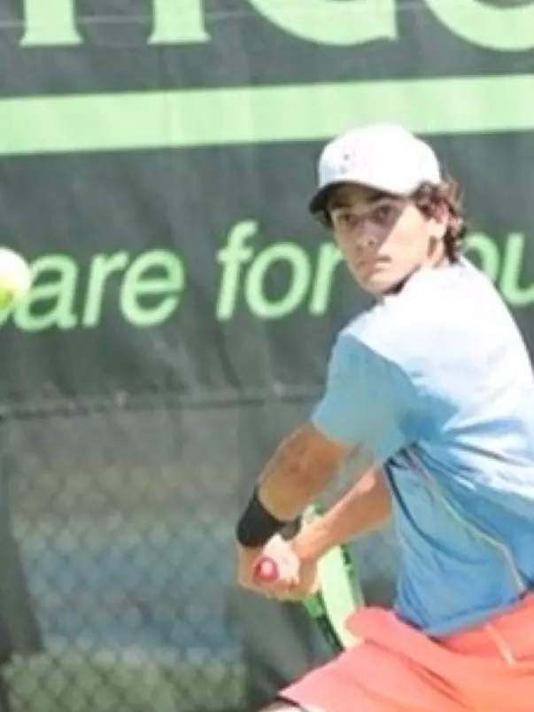 Jonah Dickson has the racket back while getting ready to swing a forehand at the tennis ball.