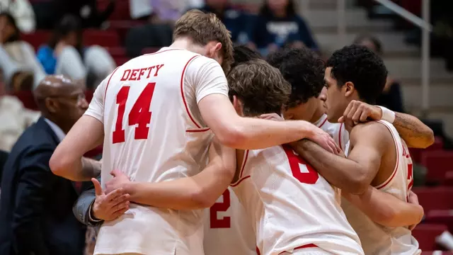 Five BU men's basketball players huddle up on the court.