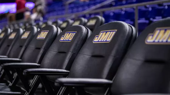 Shot of empty courtside seats displaying the JMU logo inside the Atlantic Union Bank Center.