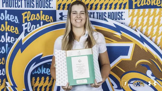 Veronika Kedronová stands smiling in front of a Kent State Golden Flashes backdrop, holding her invitation to the Augusta National Women's Amateur. The open invitation folder displays the official Augusta National crest and printed invitation inside.