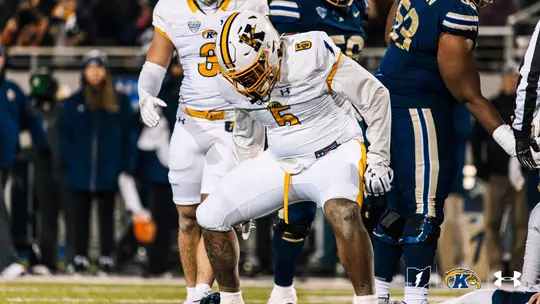 Kent State football player (#5) in a white uniform crouched down on the field during a game.