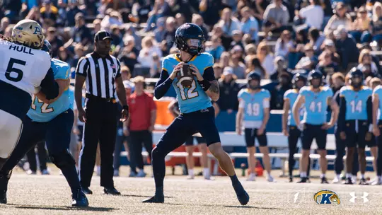 Kent State quarterback (#12) in a light blue jersey looking to throw a pass during a football game.