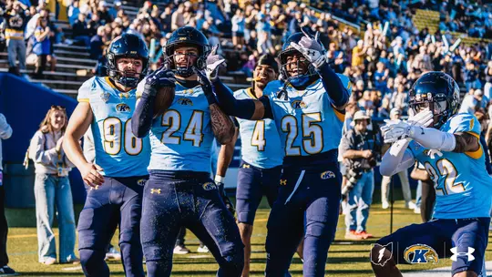 Kent State football players in light blue jerseys celebrating on the field during a game.